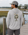 Man wearing a gray hoodie with a tree design and text on the back, standing on a dock by a body of water.