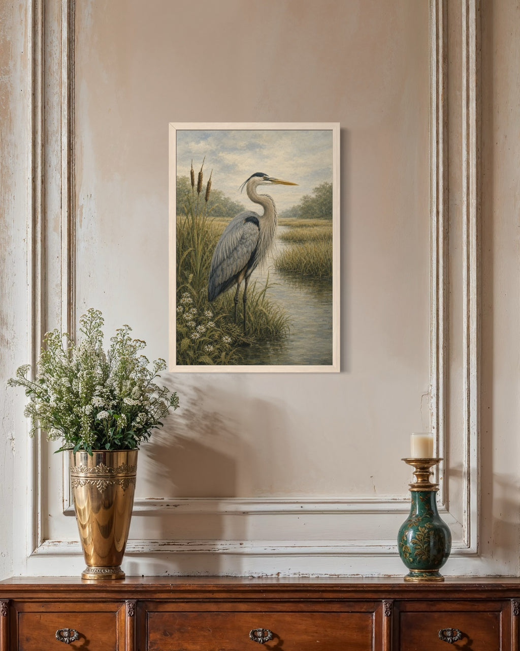 Framed nature print of a heron in a marsh on a wall above a wooden cabinet with decorative items.