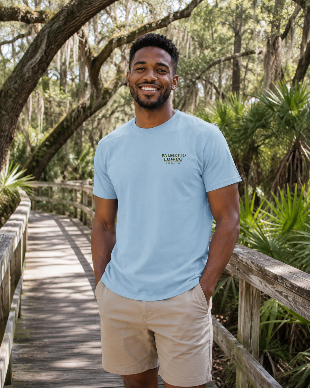Man wearing a light blue t-shirt with a logo, standing on a wooden path in a forest.
