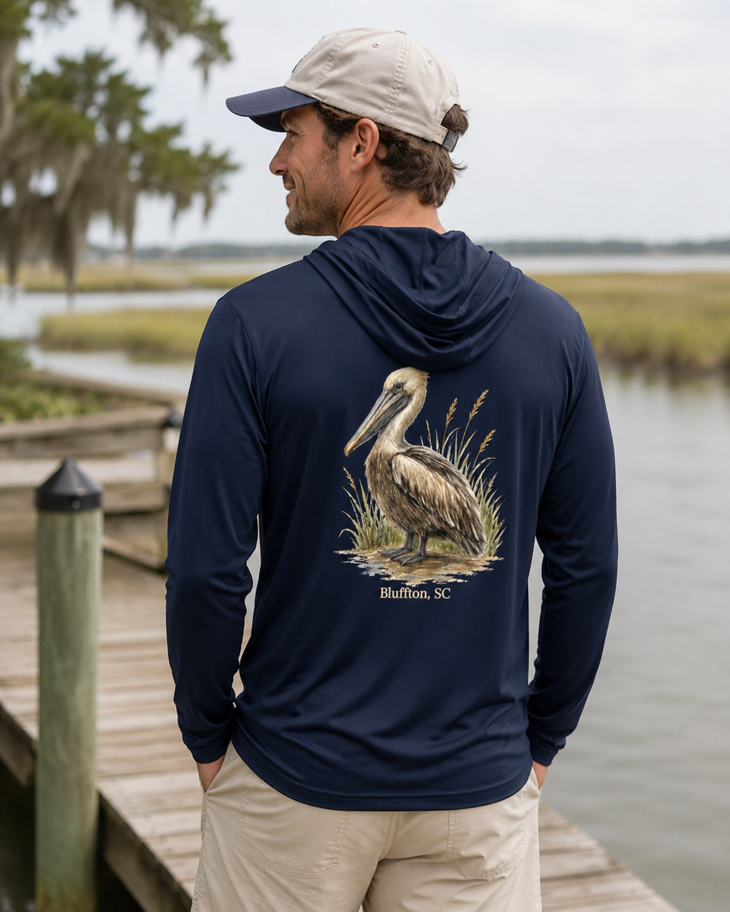 Man wearing a navy hoodie with a pelican design by a waterfront