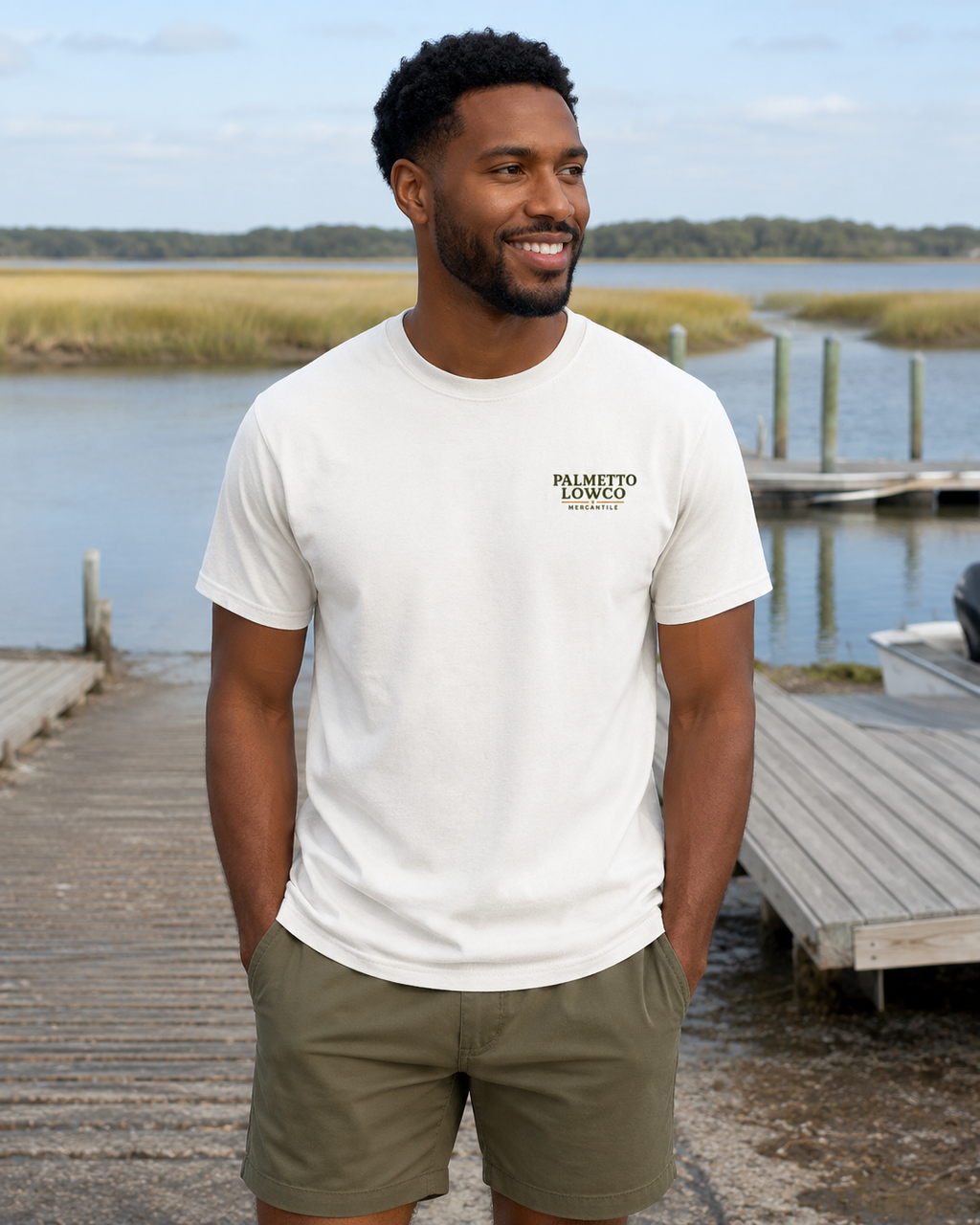 Man wearing a white t-shirt with a logo standing on a dock by a body of water.