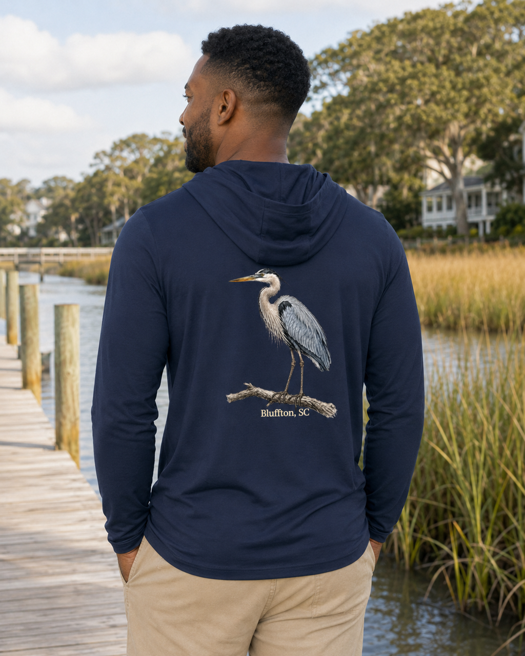 Man wearing a navy hoodie with a heron design by a waterfront
