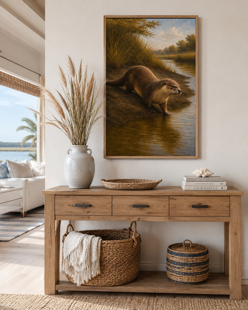 A framed landscape painting of an otter by the water, displayed on a white wall above a rustic wooden console table in a styled living room setting.