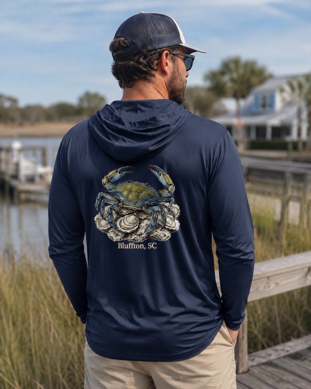 Man wearing a navy hoodie with a crab design and 'Bluffton, SC' text by a waterfront.