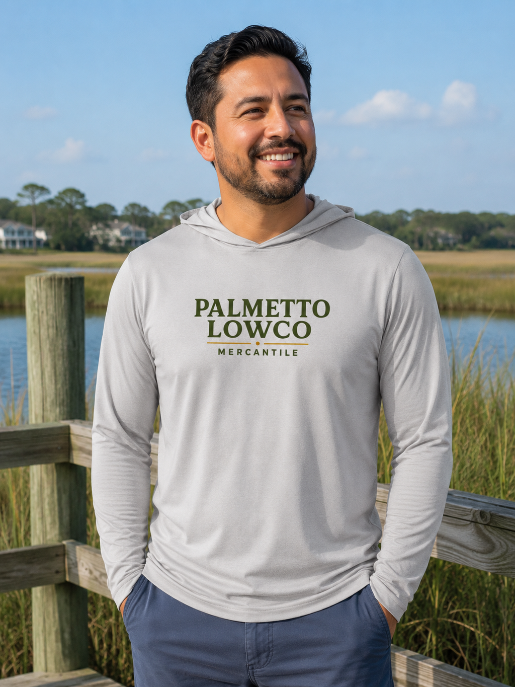 Man wearing a gray hoodie with 'Palmetto Lowco Mercantile' text, standing outdoors by a water body.
