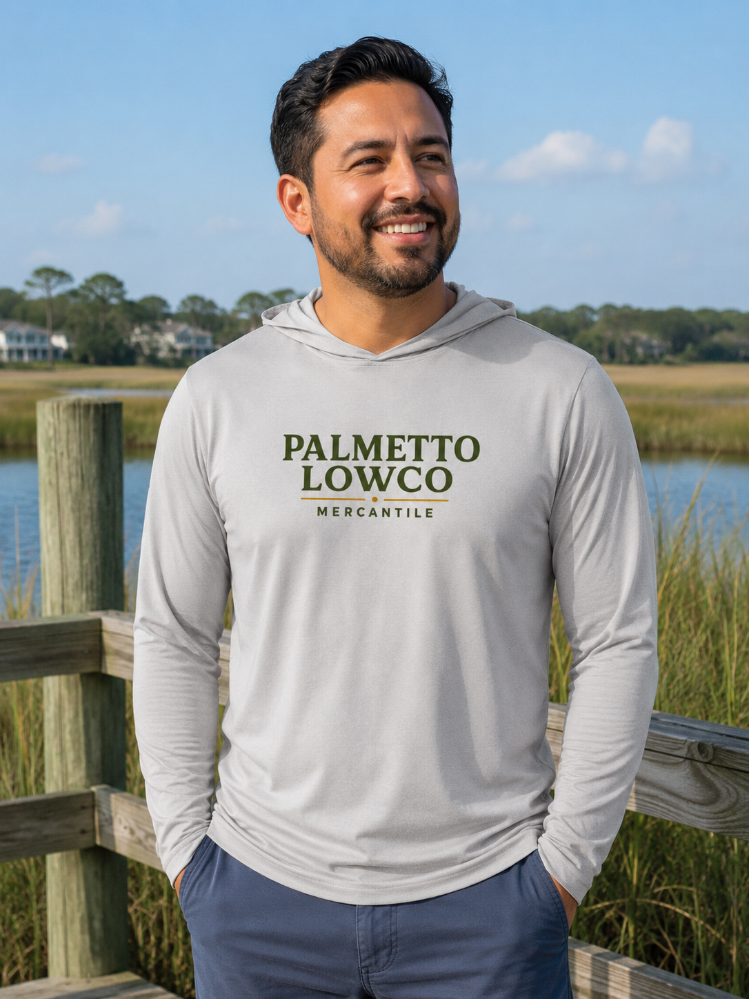 Man wearing a gray hoodie with 'Palmetto Lowco Mercantile' text, standing outdoors by a water body.