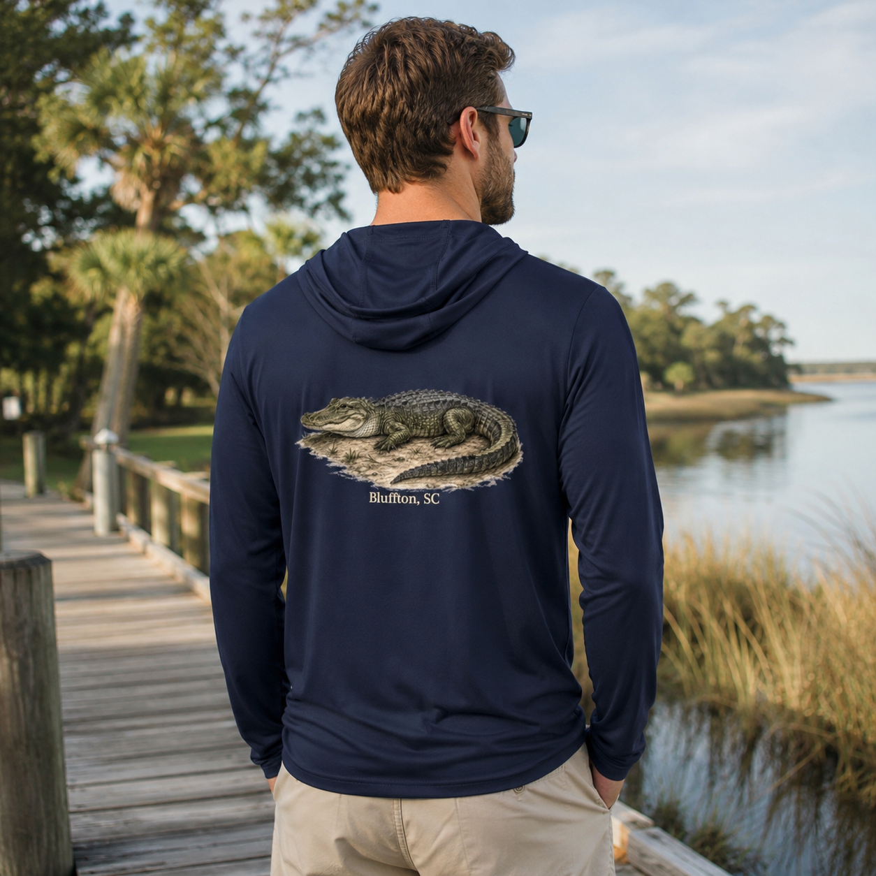 Man wearing a navy hoodie with an alligator design by a lake