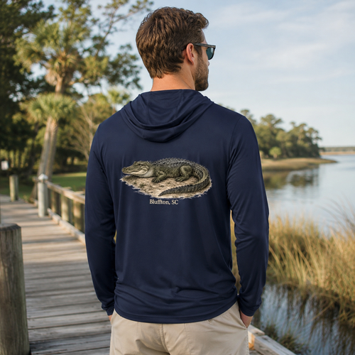 Man wearing a navy hoodie with an alligator design by a lake