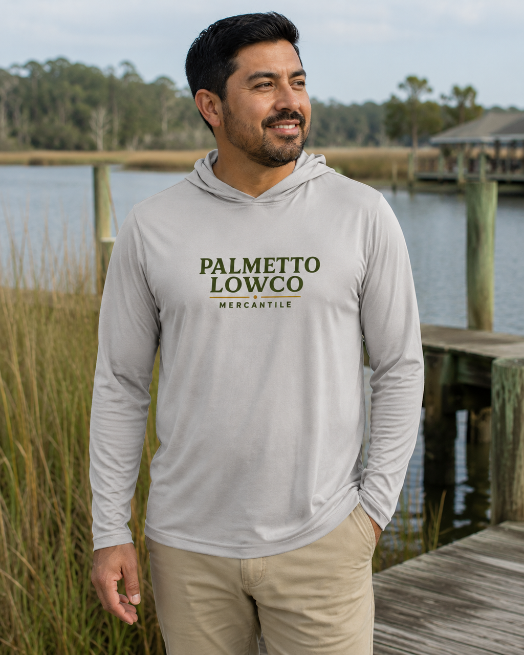 Man wearing a gray hoodie with 'Palmetto Lowco Mercantile' text, standing by a waterfront.