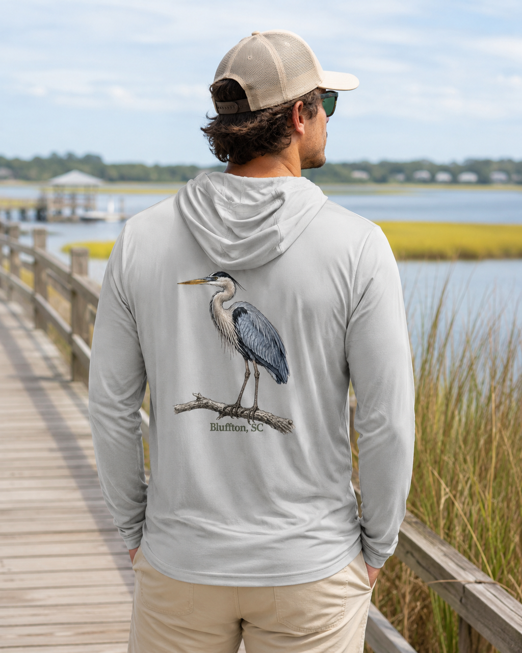 Man wearing a gray hoodie with a heron design by a waterfront