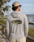 Man wearing a gray hoodie with an alligator graphic and 'Bluffton, SC' text by a waterfront.