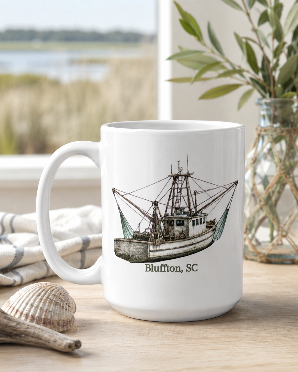 White mug with a boat illustration and 'Bluffton, SC' text on a wooden surface with a scenic background.