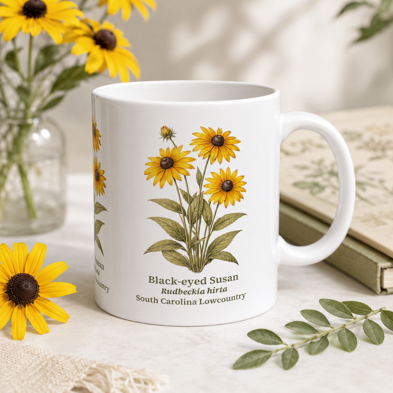 White mug with Black-eyed Susan flower design on a table with flowers and books in the background