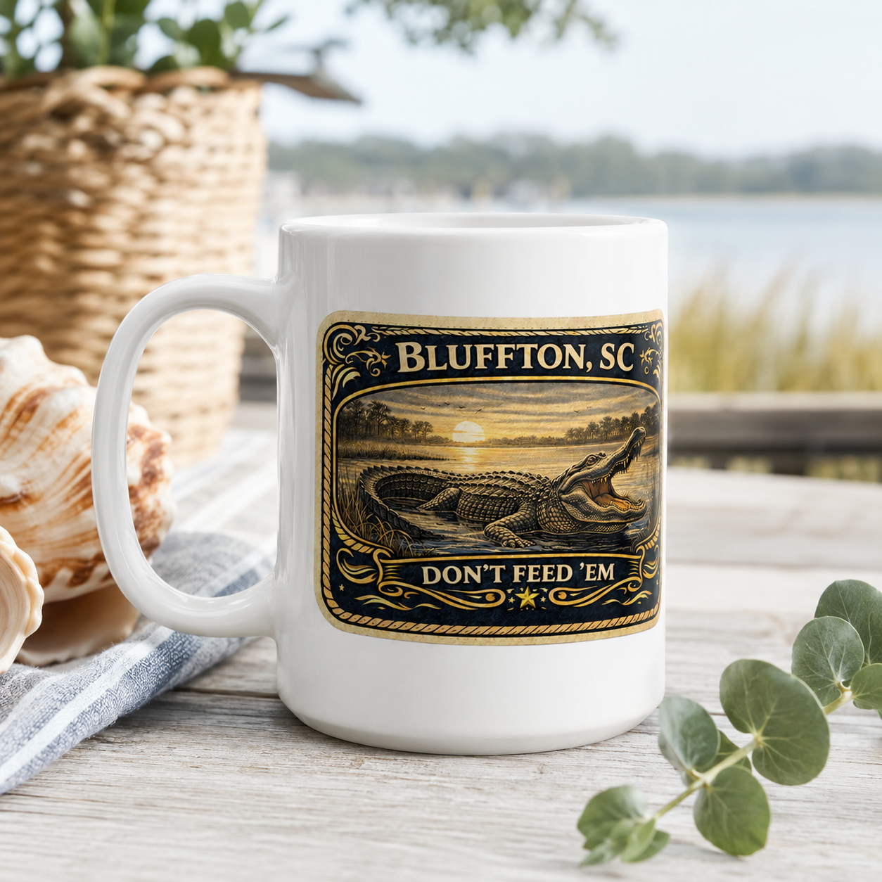 White mug with Bluffton, SC design featuring an alligator, on a wooden surface with a scenic background.