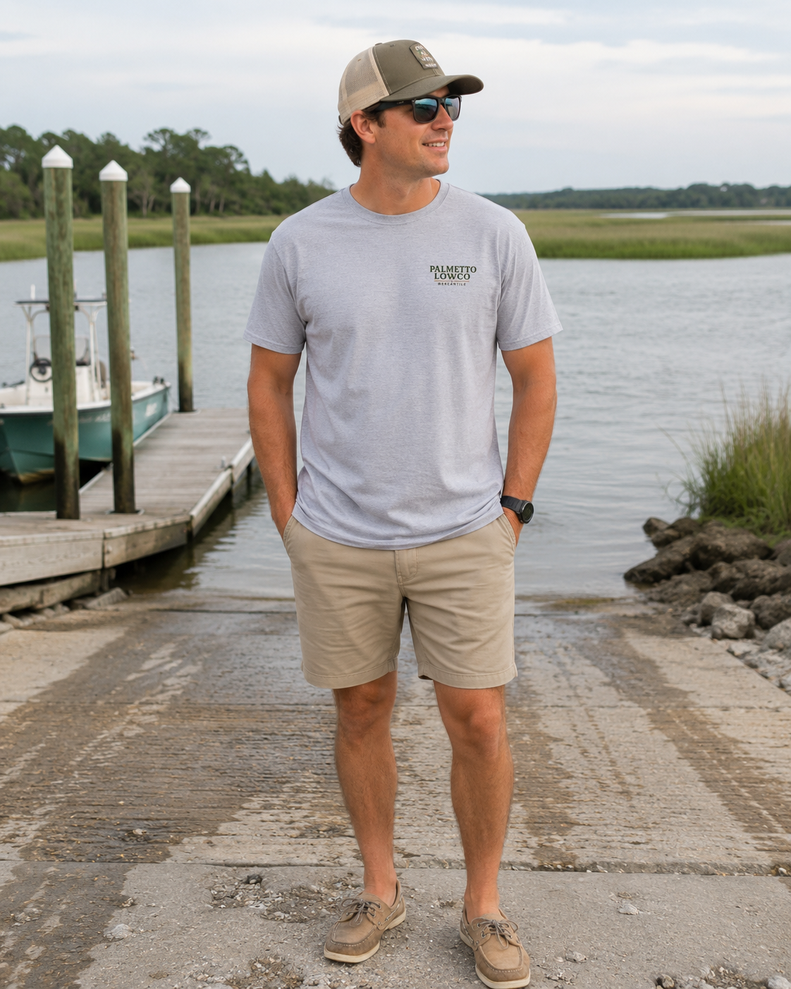 Man standing by a dock wearing a gray t-shirt with a logo and beige shorts.