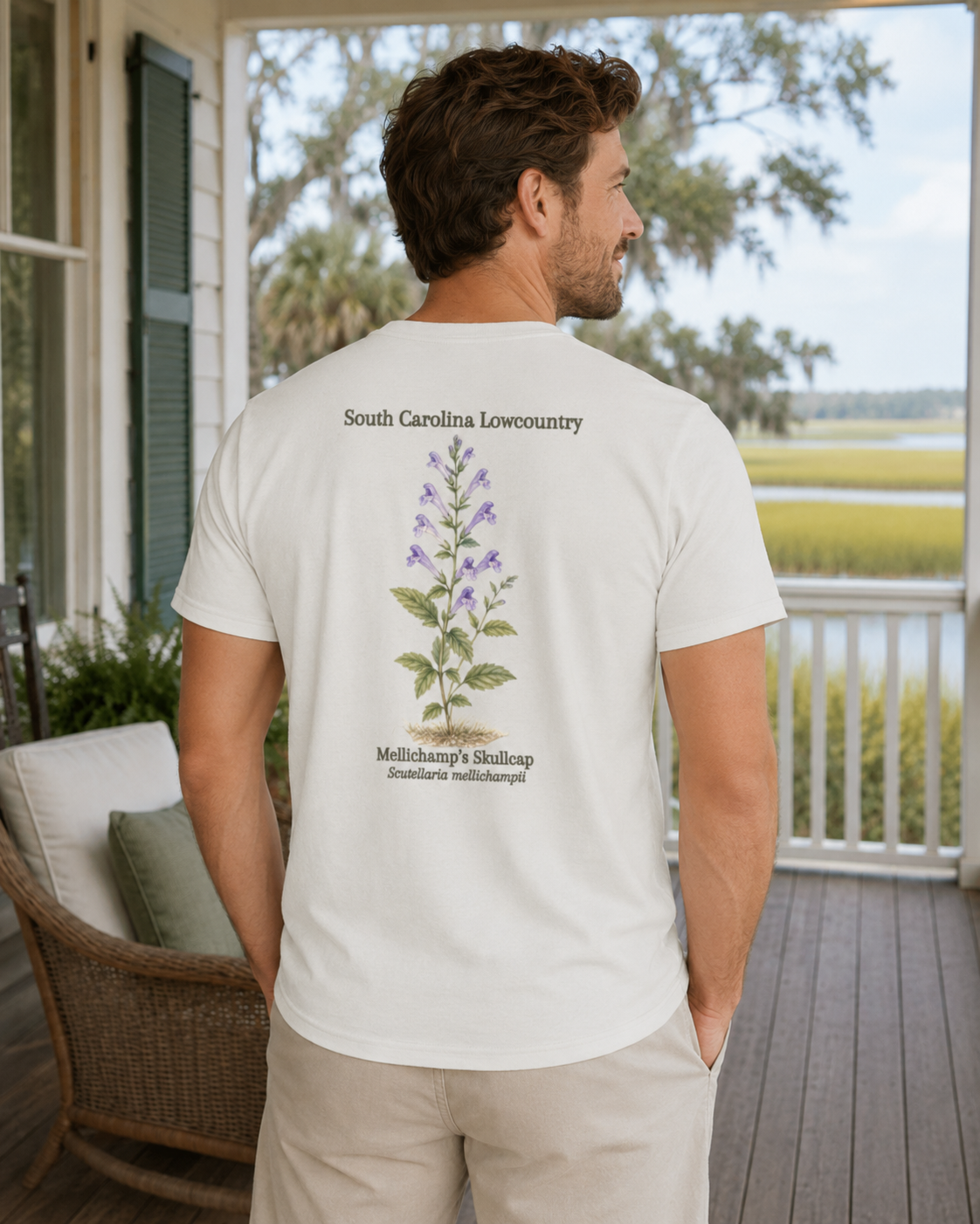 Man wearing a white t-shirt with a plant illustration and text on a porch with a scenic view.