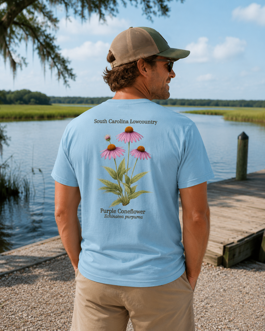 Man wearing a light blue t-shirt with a floral design and text by a body of water.