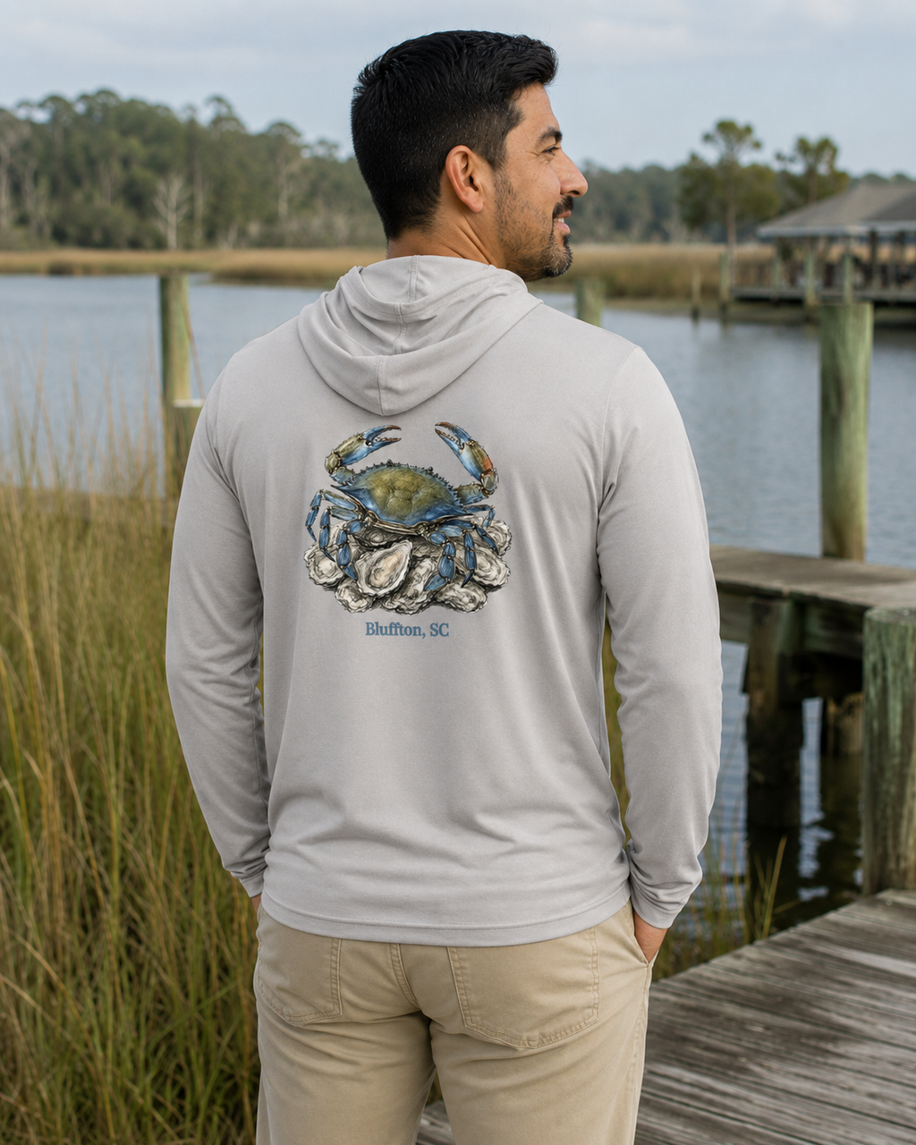 Man wearing a hoodie with a crab and oyster design by a waterfront