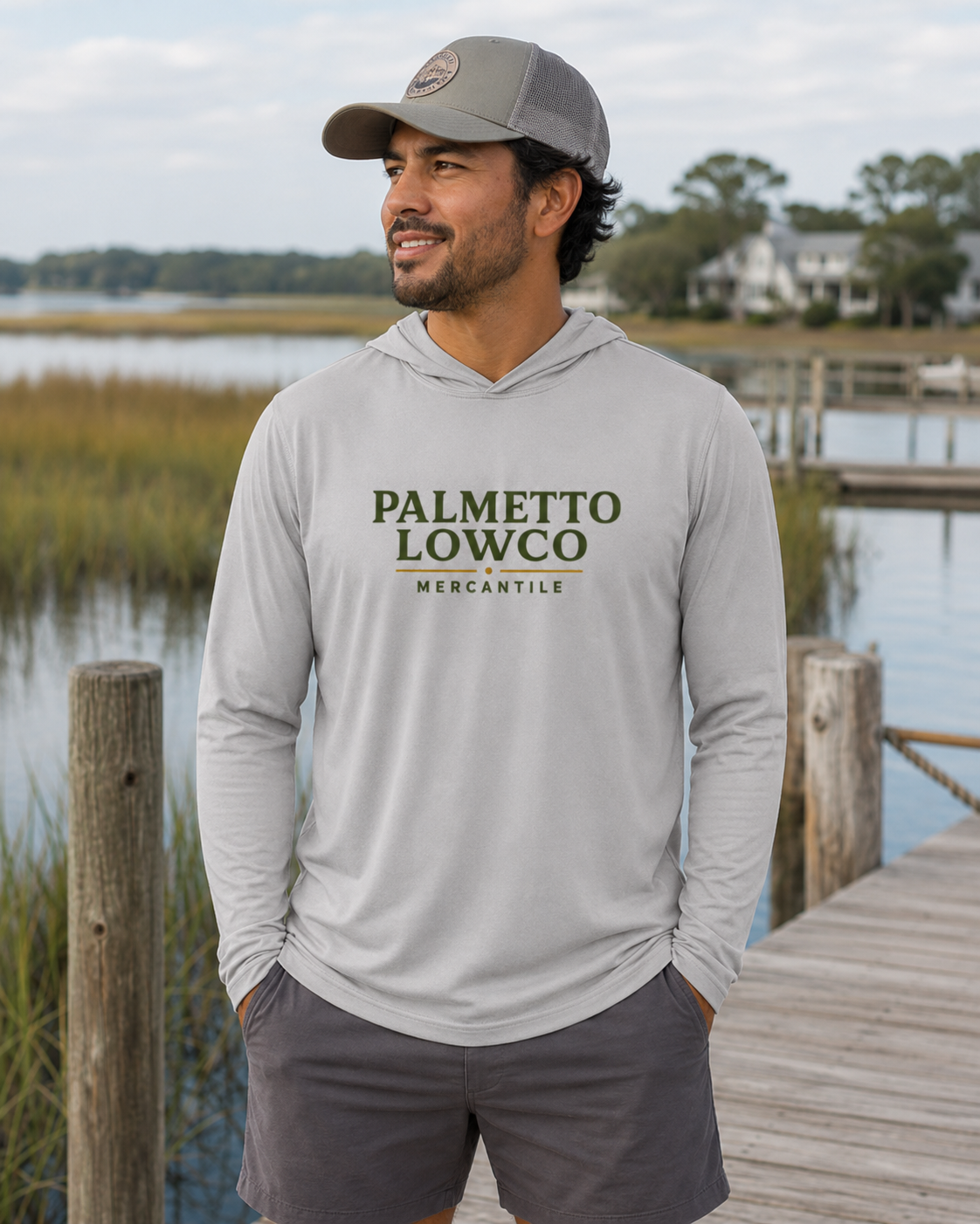 Man wearing a gray hoodie with 'Palmetto Lowco Mercantile' text by a waterfront.