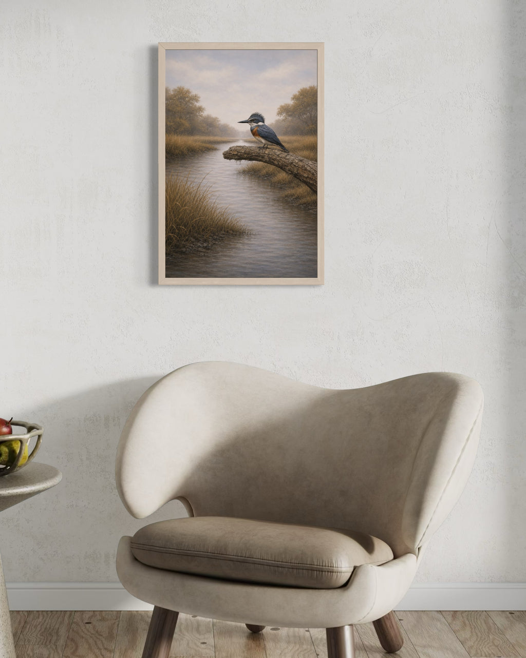 Framed artwork of a bird by a lake on a wall above a beige armchair.