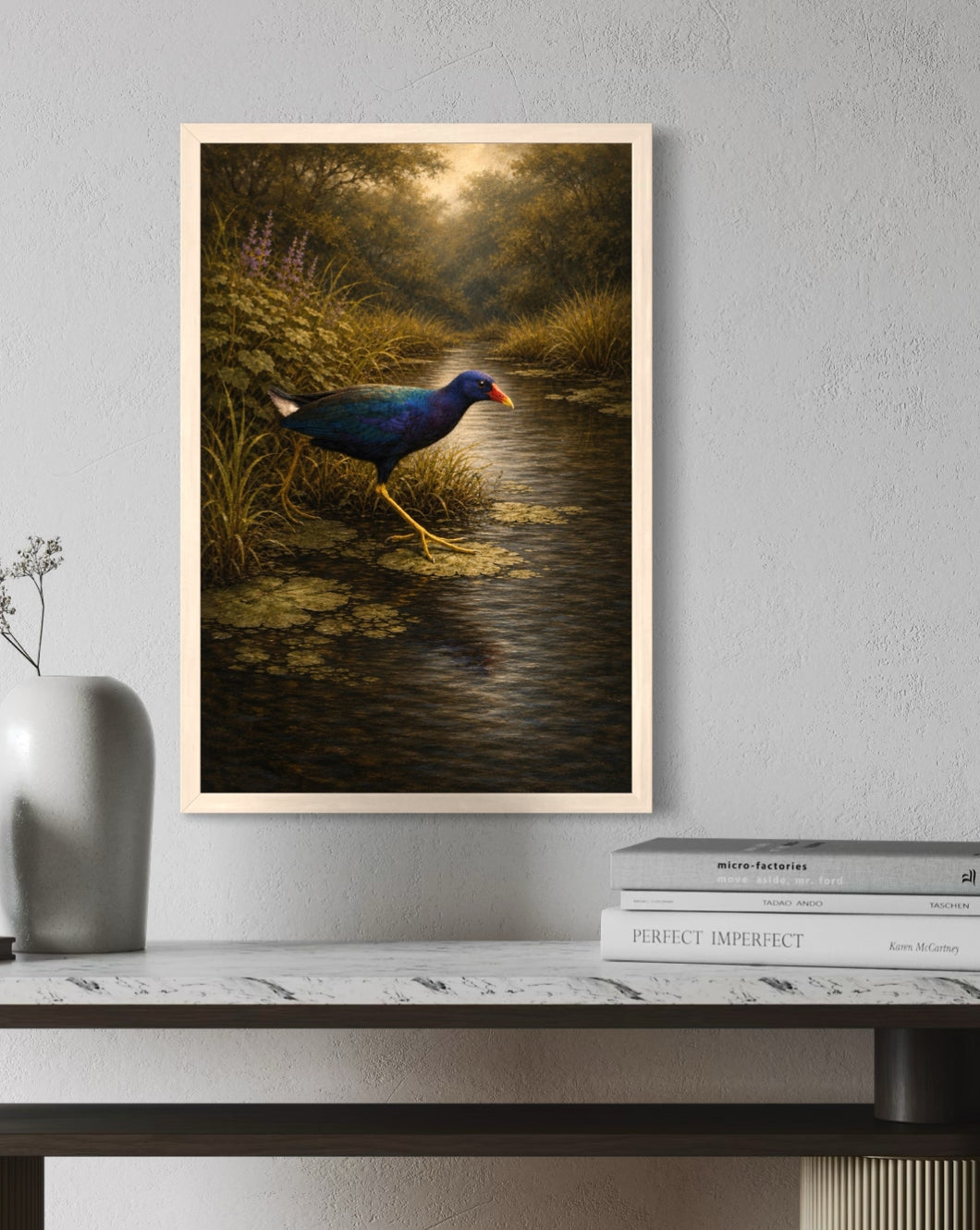 Framed painting of a bird in a natural setting on a wall above a shelf with books and a vase.